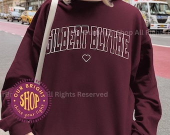 May include: Crimson-colored sweatshirt with the text "GILBERT BLYTHE" in white block letters and a small heart. The sweatshirt is a crew neck style. The word "CRIMSON" is at the bottom of the image.