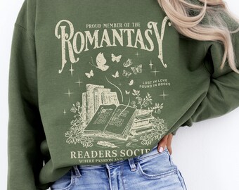 May include: A green sweatshirt with a graphic design featuring a stack of books, butterflies, and the text "Proud Member of the Romantasy Readers Society, Where Passion and Adventure Await".