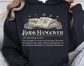 May include: Black hooded sweatshirt with a graphic print of a stack of books and the text "BOOK HANGOVER" with a definition below. The text reads: "noun (book hang-oh-verr) The struggle to return to everyday life after finishing an epic book, often accompanied by an emotional attachment to fictional characters."