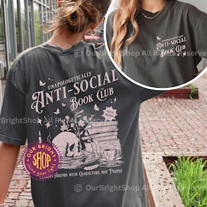 May include: Pepper-colored t-shirt with a graphic design featuring a skull, books, and the text "Unapologetically Anti-Social Book Club." The design includes butterflies and the phrase "Friends with Characters, Not People."