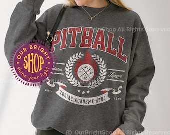 May include: Dark heather gray sweatshirt with the word "PITBALL" in red block letters. The design includes a flaming emblem, laurel wreath, and the text "Zodiac Academy Athl 2019". The sweatshirt is worn by a person wearing a white cap and sunglasses.