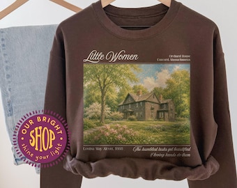 May include: A dark chocolate brown crewneck sweatshirt featuring a graphic print of a house with trees and flowers. The text reads Little Women, Orchard House, Concord, Massachusetts, Louisa May Alcott, 1868, and The humblest tasks get beautified if loving hands do them.
