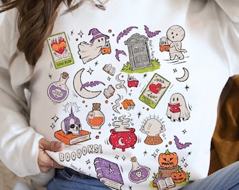 May include: White sweatshirt with a Halloween-themed graphic. The design includes ghosts, pumpkins, potion bottles, tarot cards, bats, and the text "BOOOOKS!". The sweatshirt has a crew neck and long sleeves.