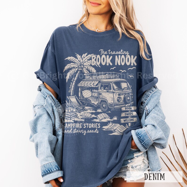 May include: A navy blue t-shirt with a graphic of a vintage van with a palm tree and the text "The traveling BOOK NOOK", "the beach", "campfire stories and starry reads", "book swaps", and "welcome".