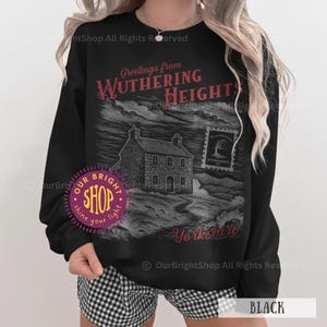 May include: Black sweatshirt featuring a graphic of a house and the text "Greetings from Wuthering Heights Yorkshire." The design is in red and gray tones. The sweatshirt has a crew neck and long sleeves.