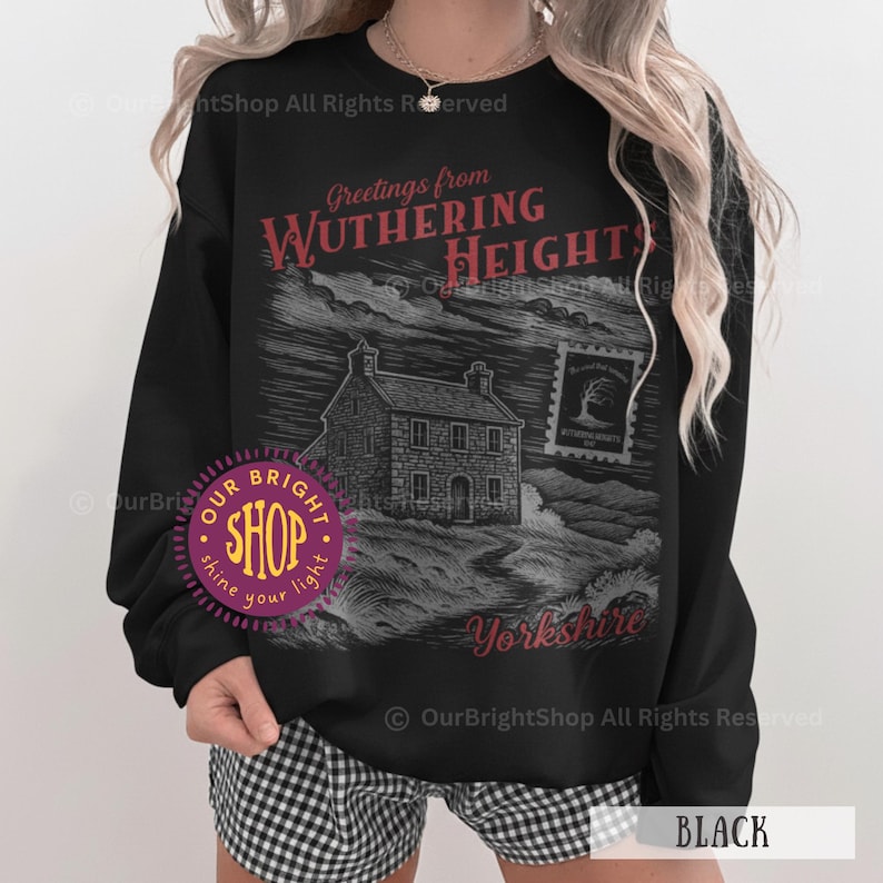 May include: Black sweatshirt featuring a graphic of a house and the text "Greetings from Wuthering Heights Yorkshire." The design is in red and gray tones. The sweatshirt has a crew neck and long sleeves.