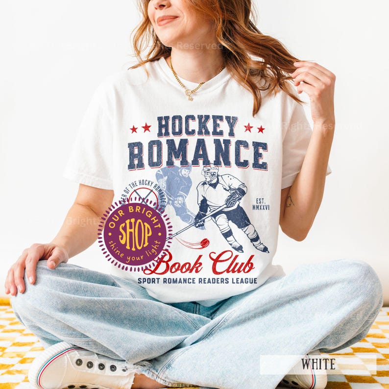 May include: White t-shirt with a Hockey Romance graphic. The design features the text "Hockey Romance" above an illustration of a hockey player. The shirt also has the text "Book Club" and "Sport Romance Readers League".
