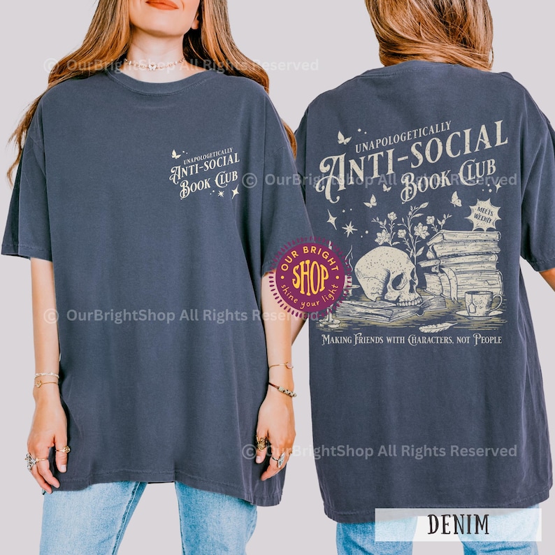 May include: Denim blue t-shirt with the text "UNAPOLOGETICALLY ANTI-SOCIAL BOOK CLUB" on the front and back. The back graphic features a skull, books, and the phrase "MAKING FRIENDS WITH CHARACTERS, NOT PEOPLE."
