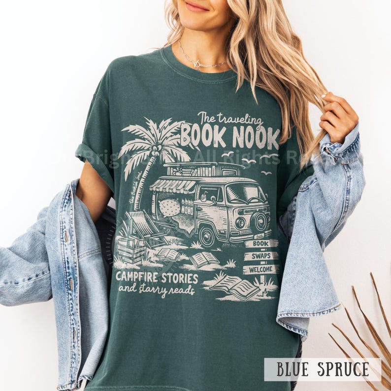May include: A teal green t-shirt with a graphic print of a vintage van with books inside. The van is parked on a beach with a palm tree and a sign that says "The Traveling Book Nook". The text "Campfire Stories and Starry Reads" is printed below the van.