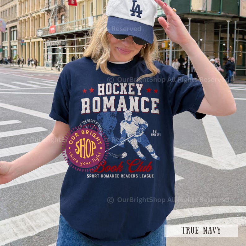 May include: True navy blue t-shirt with the text "HOCKEY ROMANCE" and a hockey player graphic. The shirt also features the text "Book Club" and "Sport Romance Readers League".
