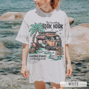 May include: White t-shirt with a graphic of a vintage camper van with the text "The traveling BOOK NOOK", "CAMPFIRE STORIES and starry reads", "BOOK SWAPS", and "WELCOME".