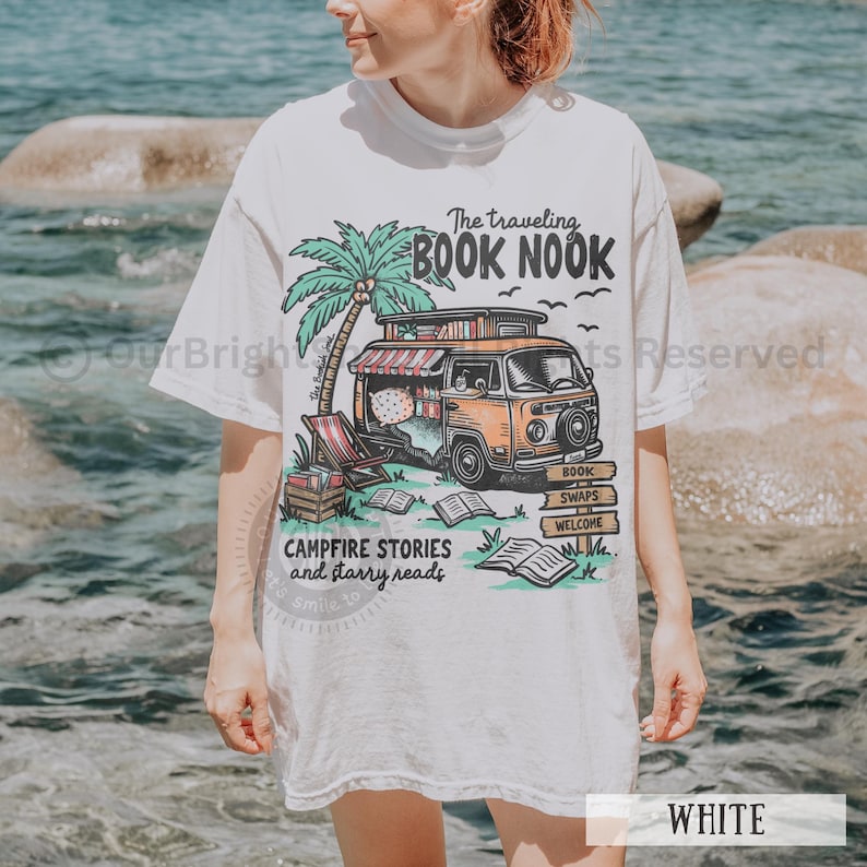 May include: White t-shirt with a graphic of a vintage camper van with the text "The traveling BOOK NOOK", "CAMPFIRE STORIES and starry reads", "BOOK SWAPS", and "WELCOME".