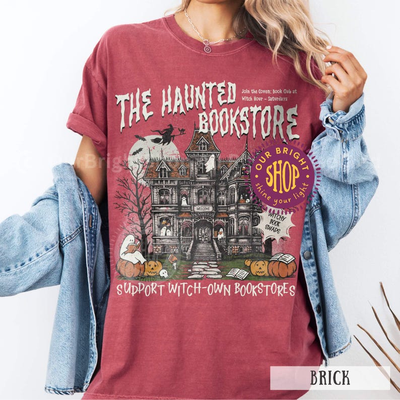 以下が含まれることがあります： レンガ色のTシャツ。お化け屋敷のグラフィックと「The Haunted Bookstore」の文字が特徴です。デザインにはカボチャ、ほうきに乗った魔女、「Support Witch-Own Bookstores」というフレーズが含まれています。