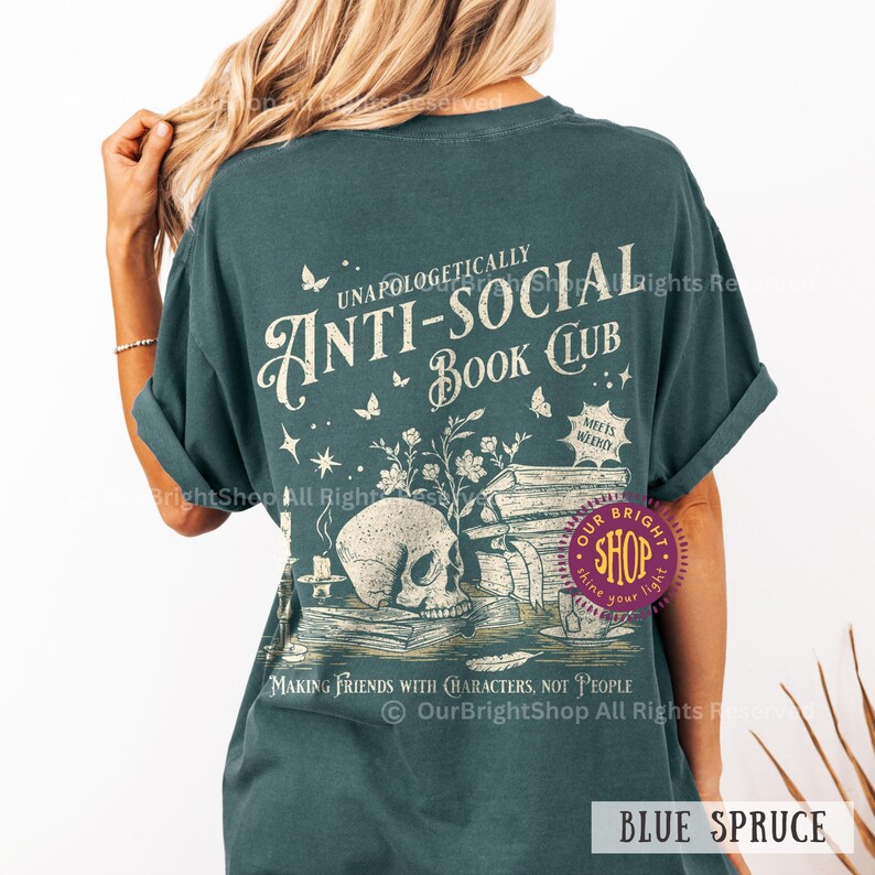 May include: Blue spruce t-shirt with the text "Unapologetically Anti-Social Book Club." The design features a skull, books, butterflies, and the phrase "Making Friends with Characters, Not People."