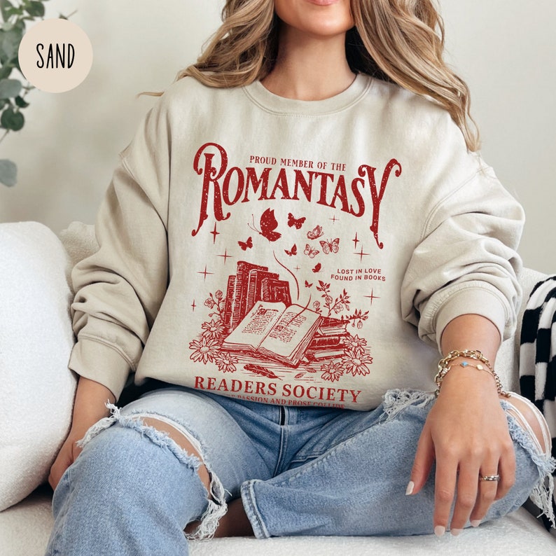 May include: A beige sweatshirt with a red graphic print of a stack of books, butterflies, and the text "Proud Member of the Romantasy Readers Society - Passion and Prose Collective - Lost in Love Found in Books".