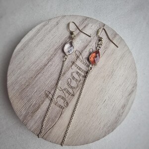 May include: A pair of long, delicate earrings with a teardrop-shaped clear crystal and a teardrop-shaped orange crystal.