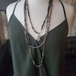 May include: A layered necklace with a teardrop-shaped pendant. The necklace is made of green, brown, and silver beads.