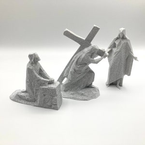 Puede incluir: Tres figuras grises de piedra que representan una escena de la Vía Crucis. Las figuras son de una persona arrodillada, una persona que lleva una cruz y una persona de pie con los brazos extendidos.