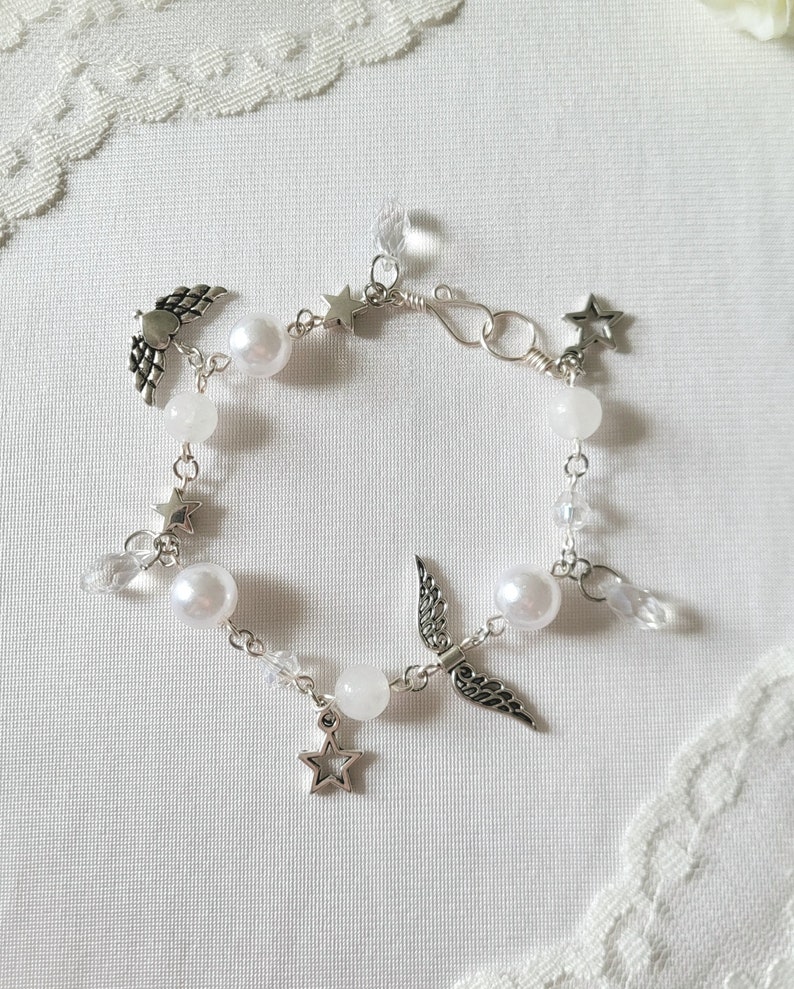 Puede incluir: Un brazalete de perlas blancas y cristal con dijes de plata de alas y estrellas.