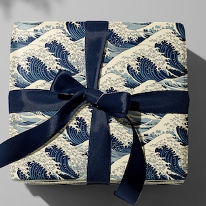 Pode incluir: Uma caixa de presente embrulhada em papel com padrão de ondas azuis e brancas com uma fita de cetim azul marinho amarrada em um laço.