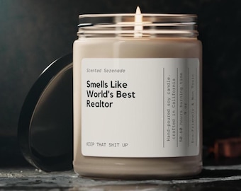 Könnte beinhalten: Eine brennende Sojakerze in einem klaren Glasgefäß mit schwarzem Deckel. Das weiße Etikett trägt die Aufschrift: Scented Serenade, Smells Like World's Best Realtor, KEEP THAT SHIT UP, Hand-poured soy candle, crafted in California, 50-60 hours burning time, 255g, Eco-Friendly & Non Toxic.