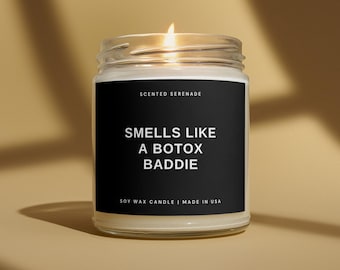 May include: A clear glass jar soy wax candle with a lit wick. The black label features the white text Scented Serenade, Smells Like A Botox Baddie, and Soy Wax Candle | Made In USA. The candle emits a warm glow from the flame at the top.