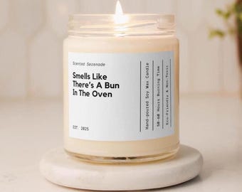 May include: A lit soy wax candle in a clear glass jar with a white label reading Scented Serenade, Smells Like There's A Bun In The Oven, Est. 2025, Hand-poured Soy Wax Candle, 50-60 Hours Burning Time, and Eco-Friendly & Non-Toxic.