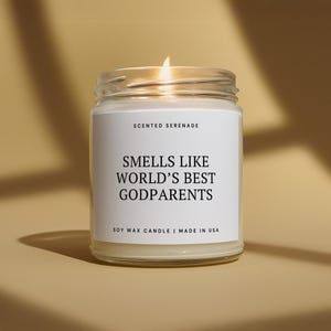 May include: A lit soy wax candle in a glass jar with a white label. The label reads "Smells Like World's Best Godparents" and "Scented Serenade". The candle is made in the USA.