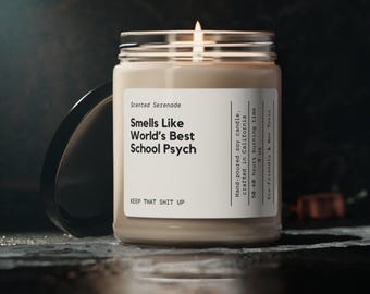 May include: A beige soy candle in a clear glass jar with a black lid. The white label reads: Scented Serenade, Smells Like World's Best School Psych, KEEP THAT SHIT UP, Hand-poured soy candle, crafted in California, 50-60 hours burning time, 255g, Eco-Friendly & Non Toxic.