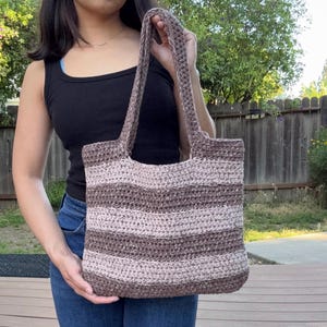 May include: A handmade crochet tote bag in shades of brown and tan. The bag features horizontal stripes and sturdy handles. This stylish and practical bag is perfect for carrying everyday essentials.