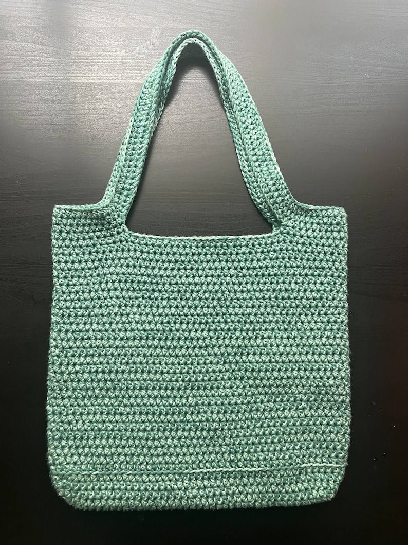 May include: A teal crocheted tote bag with two straps. The bag is made with a simple stitch pattern.