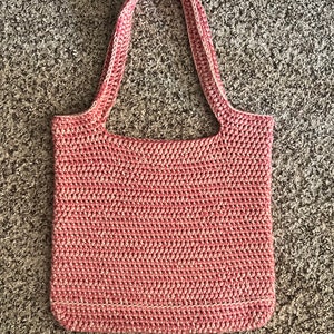 May include: A pink and white crocheted tote bag with a single handle.