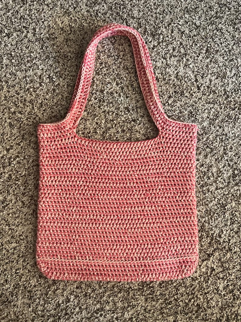 May include: A pink and white crocheted tote bag with a single handle.