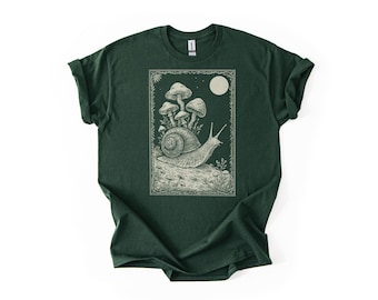 May include: Dark green t-shirt featuring a detailed illustration of a snail carrying mushrooms on its back, under a full moon. The design is framed with a decorative border. The shirt is made of a soft material.