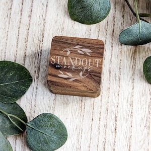 May include: A wooden box with a light brown finish and a floral design engraved on the top. The box has the text "STANDOUT MOCKUPS" engraved on the top. The box is sitting on a white wooden surface.