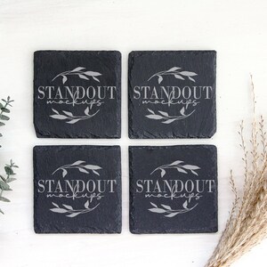 May include: Four black slate coasters with a white design that says "Standout Mockups".