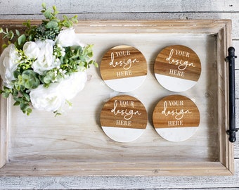 Puede incluir: Cuatro posavasos redondos de madera con la mitad inferior blanca y el texto "YOUR design HERE" en escritura blanca. Los posavasos están colocados en una bandeja de madera con un ramo de flores blancas y vegetación.