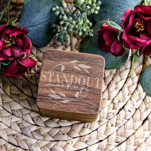 May include: A wooden box with the text "STANDOUT mockups" engraved on the top. The box is sitting on a woven straw mat with red roses and green leaves.
