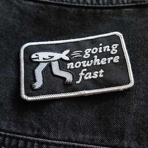 May include: A black and white embroidered patch with a cartoon figure running and the text "going nowhere fast".