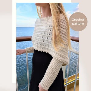 Op de afbeelding: Een crèmekleurige, gehaakte trui-sjaal met lange mouwen, voorzien van een gestructureerd ribpatroon en een delicate geschulpte rand langs de halslijn. Het kledingstuk is gelabeld als Frost & Fern Sweater Scarf en Crochet pattern.