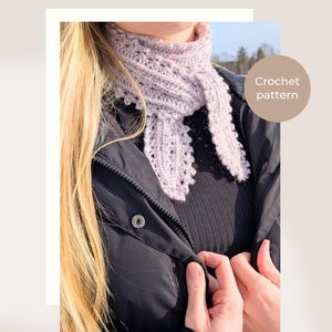 Op de afbeelding: Een lichtpaarse gehaakte mini-sjaal met een delicaat openwerk patroon. De sjaal wordt over een zwarte jas gedragen. De tekst "Frost & Fern Mini Scarf" en "Crochet pattern" is zichtbaar.