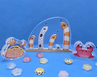 May include: Acrylic sea creature decorations, including a crab, a sea slug, and a group of orange and white striped eel-like figures. The scene is set against a blue background with scattered gems and gold accents.