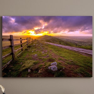May include: A scenic landscape photograph featuring a wooden fence along a dirt path leading to a hilltop with a dramatic sunset sky in the background.