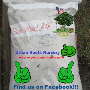 May include: A white plastic bag filled with gray wood ash. The bag has a label that says "Pure Wood Ash" and "Urban Roots Nursery". The label also has a small American flag and a green tree with a red birdhouse. The bag has a green thumbs up icon and the text "We give you green thumbs up!!!" and "Find us on Facebook!!!".