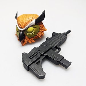 May include: A black plastic toy gun with a magazine and a brown and orange owl mask.