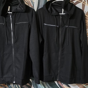 Puede incluir: Dos chaquetas negras con capucha y cremallera, con bolsillos con cremallera y capucha con cordón.
