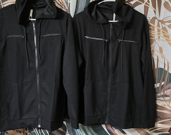 May include: Two black hooded zip-up jackets with zippered pockets and a drawstring hood.