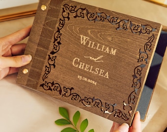 May include: A wooden photo album with a decorative, intricate design carved into the cover. The album is personalized with the names "William and Chelsea" and the date "23.10.2024".