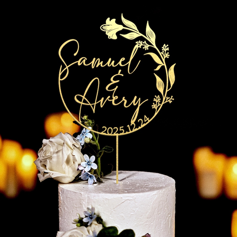 K&ouml;nnte beinhalten: Goldener Hochzeitstortenaufsatz mit floralem Design und den Namen Samuel & Avery sowie dem Datum 2025.12.24.