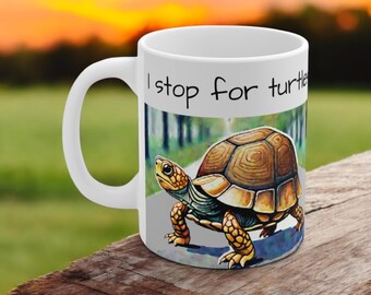 Może przedstawiać: Biały ceramiczny kubek do kawy z ilustracją brązowego i żółtego żółwia i tekstem "I stop for turtles".